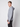 A young man with short light brown hair models the PROJEK RAW Mens Long Sleeve Hoodie with Kangaroo Pocket in light grey, paired with dark pants, standing sideways and looking toward the camera against a plain background.