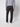 A person stands facing away from the camera against a plain light background, wearing PROJEK RAW Men’s 5-Pocket Pant in black stretch fabric, paired with a gray long-sleeve shirt and white sneakers.