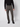 A man stands against a plain light background, wearing a black long-sleeve shirt, PROJEK RAW Men’s Relaxed Chino Pant in gray, and black shoes. His face is not visible in the image.