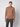 A young man stands against a plain light background, wearing the PROJEK RAW Mens Half-zip Cashmere Touch Sweater in brown with dark grey pants, his expression neutral and arms relaxed by his sides.