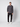 A young man wears the PROJEK RAW Mens Casual Dress Shirt with Logo Detail in dark gray, styled with black pants and white sneakers. He faces forward, one hand in his pocket, showing off the shirts modern, versatile look.