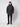 A person stands facing forward against a plain light background, wearing the PROJEK RAW Mens Textured Ripstop Ecofill Quilted Parka with Hood in black, paired with black pants and black boots.