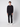 A young man stands facing forward against a plain light background, wearing a black long-sleeve sweater, PROJEK RAW Mens 5-Pocket Flex Knit Jeans, and white sneakers. His arms rest relaxed at his sides.
