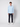 A man stands against a white background wearing the PROJEK RAW Mens 24/7 Button-up Shirt in light blue, paired with dark pants and white sneakers. He faces forward with a neutral expression.