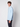 A young man with curly brown hair wears the PROJEK RAW Mens 24/7 Button-up Shirt in light blue and dark pants, standing sideways and looking at the camera against a plain light background.