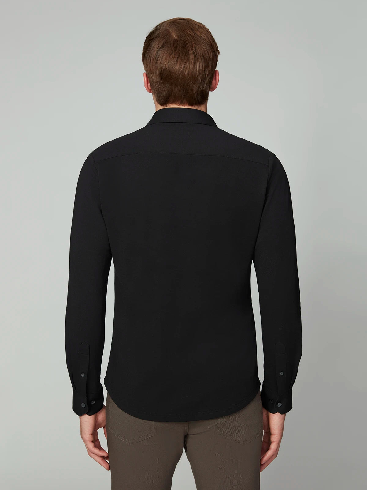 A man with short brown hair stands with his back to the camera, wearing the PROJEK RAW MENS 24/7 BUTTON-UP KNIT SHIRT and dark brown pants against a plain light gray background.