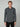 A man with short blonde hair models the PROJEK RAW MENS 24/7 BUTTON-UP KNIT SHIRT in dark gray with black pants, standing against a light gray background and looking directly at the camera with a neutral expression.