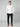A man faces forward against a plain light background, wearing the PROJEK RAW MENS 24/7 BUTTON-UP KNIT SHIRT in white, dark pants, and brown loafers, with his left hand in his pocket.