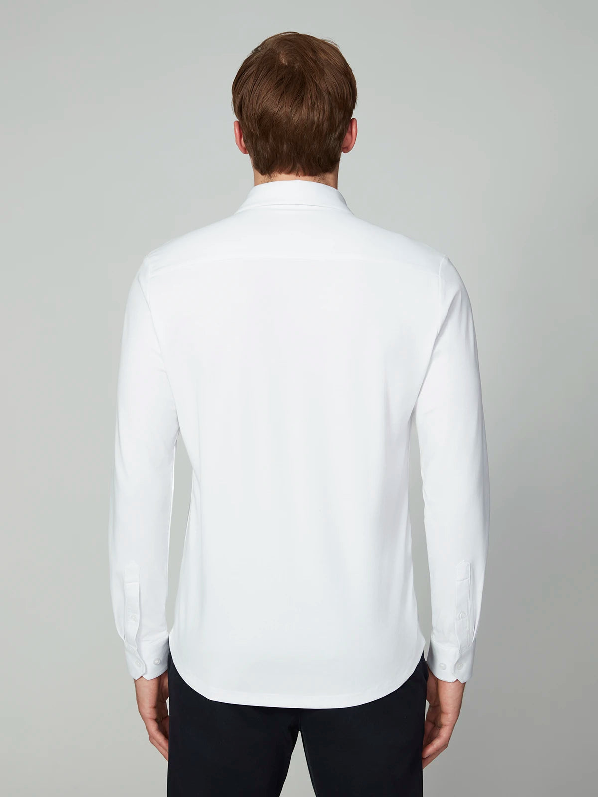 A man with short brown hair stands with his back to the camera, wearing the MENS 24/7 BUTTON-UP KNIT SHIRT by PROJEK RAW and black pants, set against a light gray background.