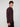 A young man with curly brown hair models the PROJEK RAW MENS LONG SLEEVE 4WAY STRETCH TWILL SHIRT in burgundy and black pants, standing sideways and looking at the camera against a plain light gray background.