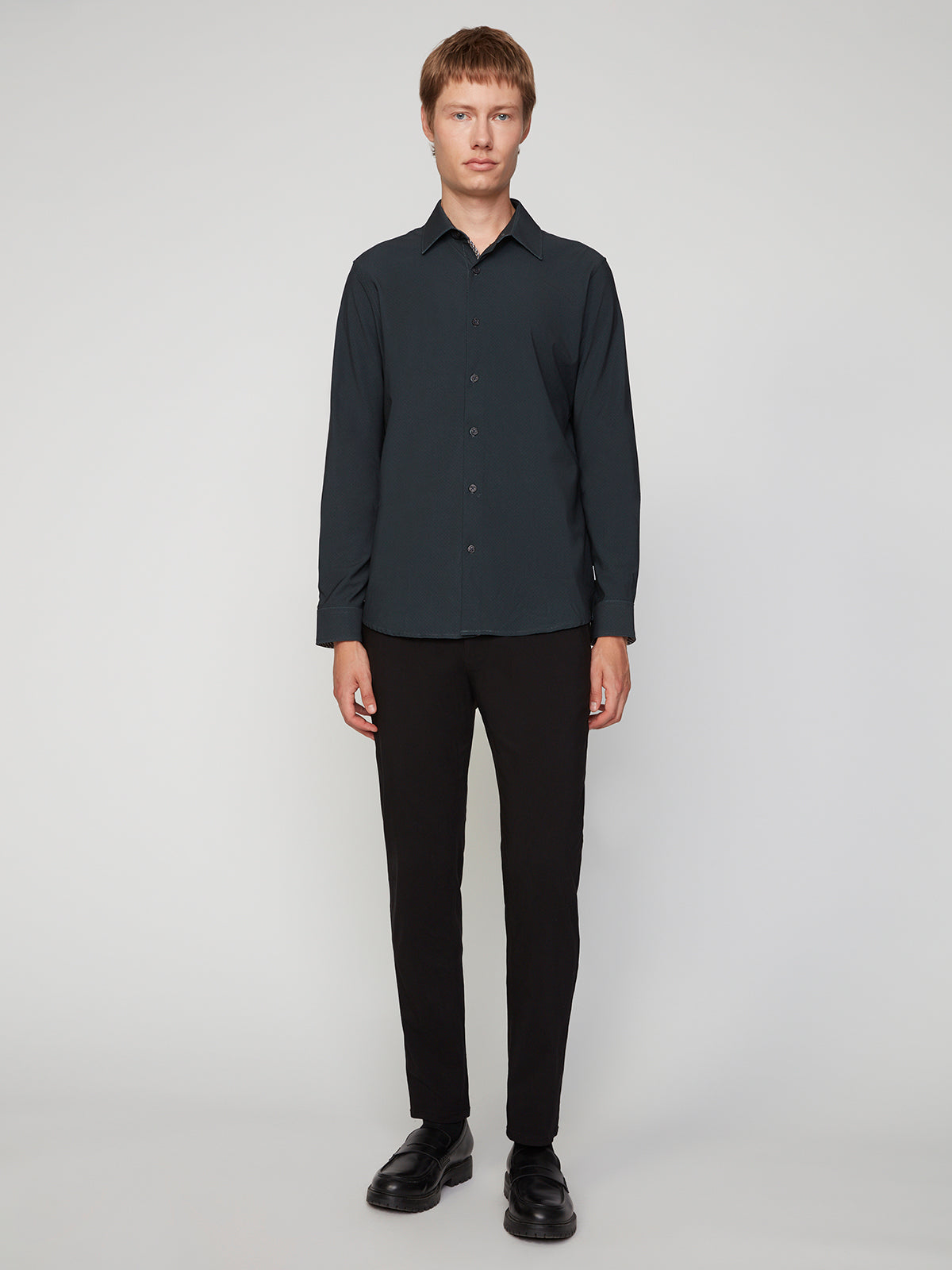A person with light skin and short brown hair faces forward, wearing the PROJEK RAW MENS LONG SLEEVE 4WAY STRETCH TWILL SHIRT, paired with black pants and black shoes against a plain light background.