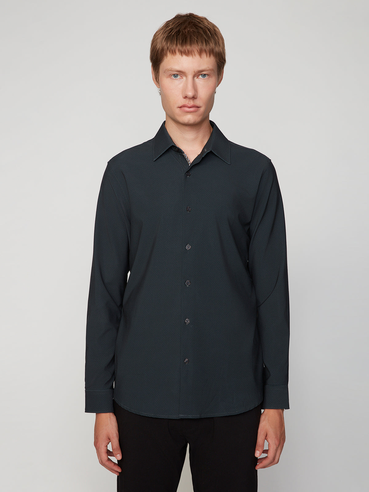 A young man with short light brown hair wears a black PROJEK RAW MENS LONG SLEEVE 4WAY STRETCH TWILL SHIRT, standing facing the camera against a plain light gray background.