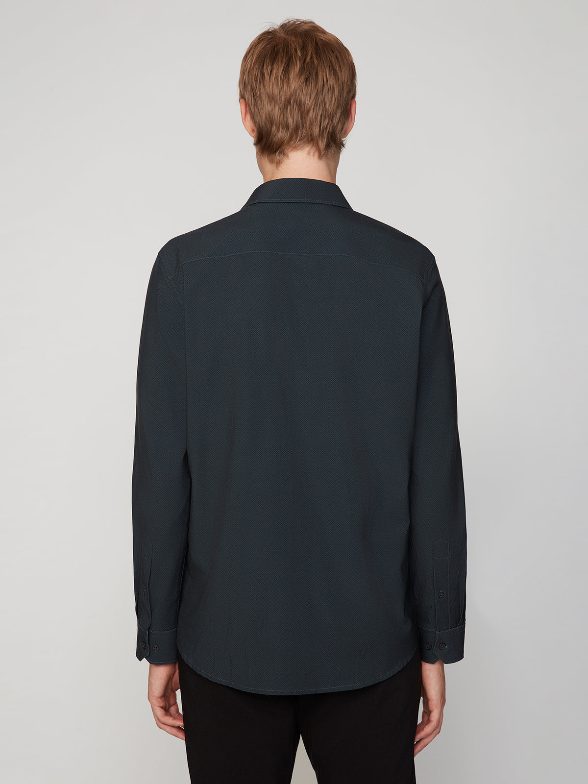 A person with short, light brown hair is seen from behind wearing the PROJEK RAW MENS LONG SLEEVE 4WAY STRETCH TWILL SHIRT and black pants against a plain light background.